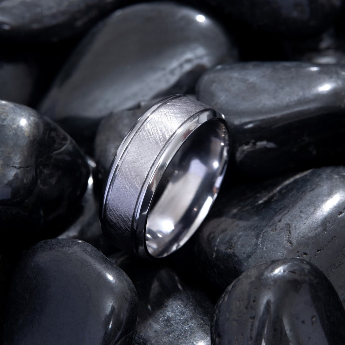Bague Ravenstone en tantale brossé, posée sur des pierres noires lisses.