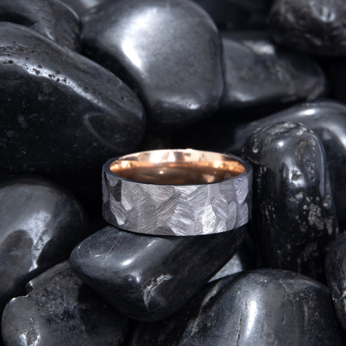 Bague Ravenstone en tantale gris brossé avec intérieur en or rose poli, posée sur des pierres noires lisses.