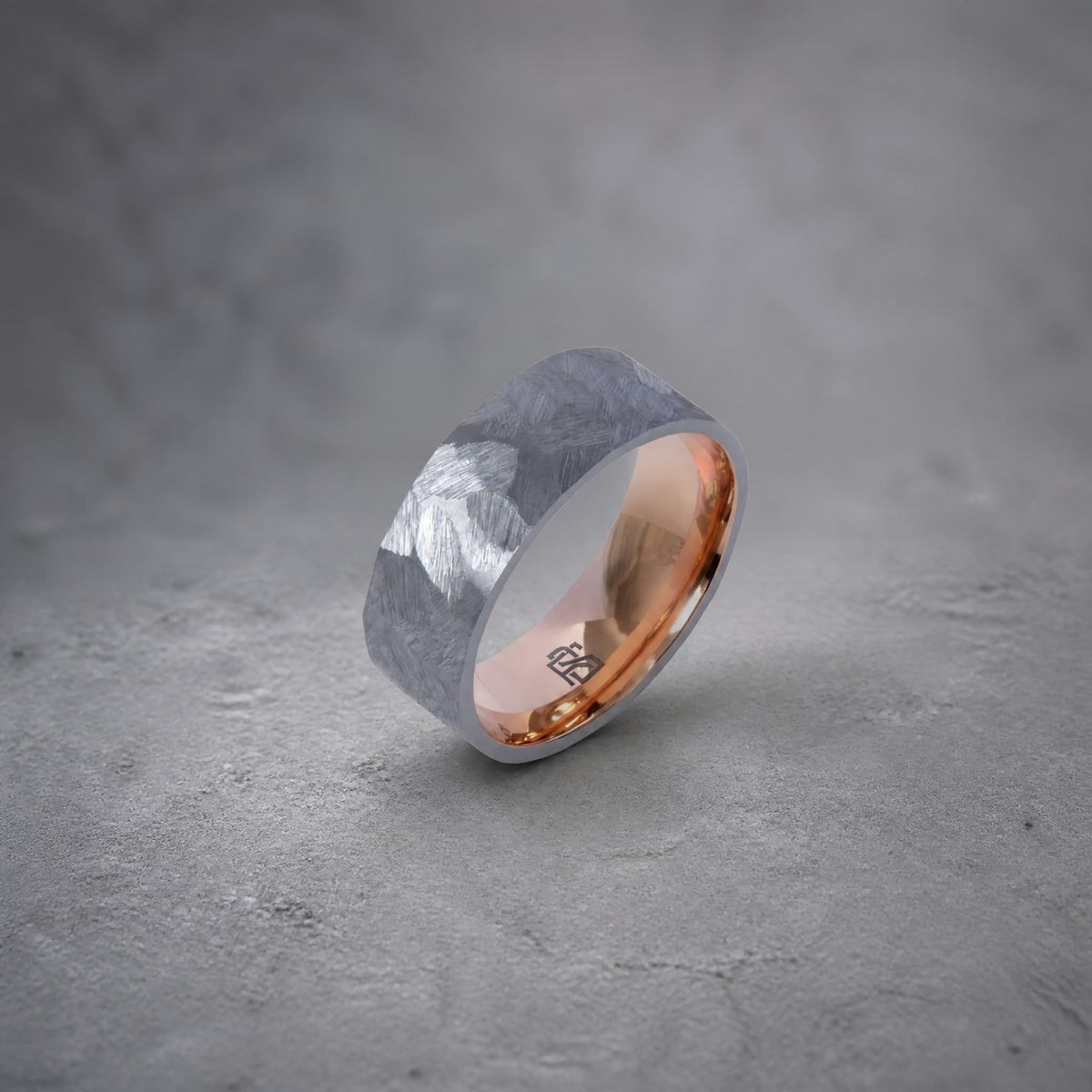 Bague Ravenstone en tantale gris brossé avec intérieur en or rose poli, posée sur un fond gris texturé.