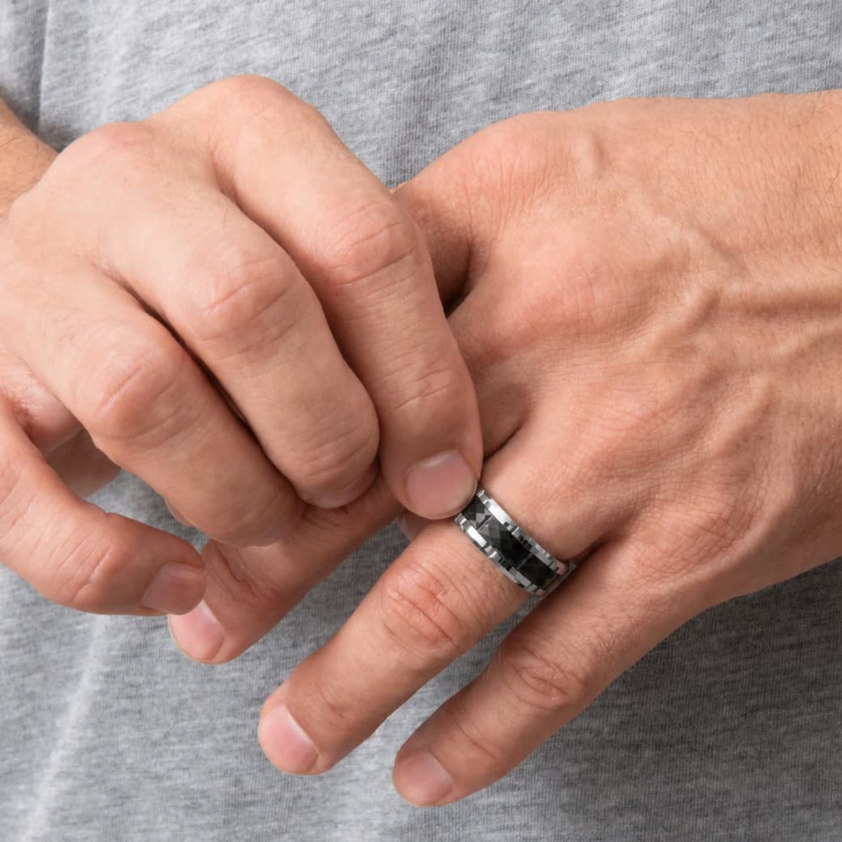 Bague Ravenstone en tungstène facettée noire avec bord argenté, portée aux mains dans une scène minimaliste.