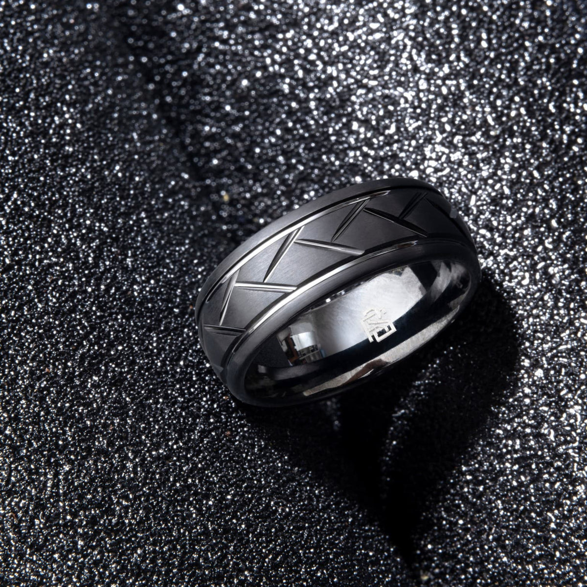 Bague masculine en tungstène noir Ravenstone, motif géométrique gravé, mise en scène sur texture minérale noire pour un rendu technique et luxueux.
