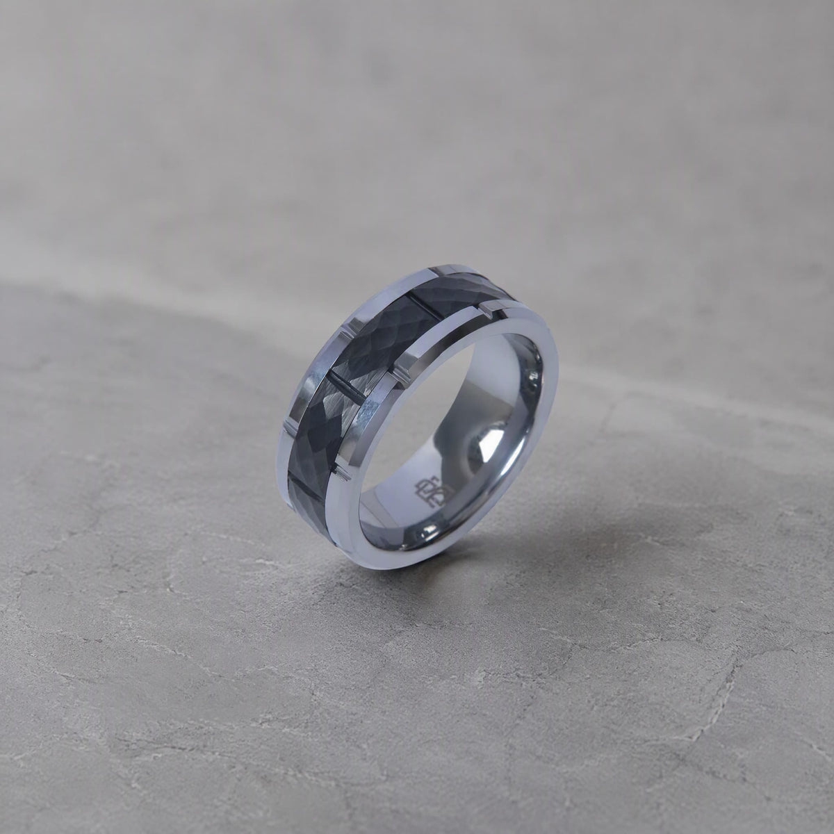 Bague Ravenstone en tungstène noir avec insert facetté argent, présentée sur fond gris texturé.