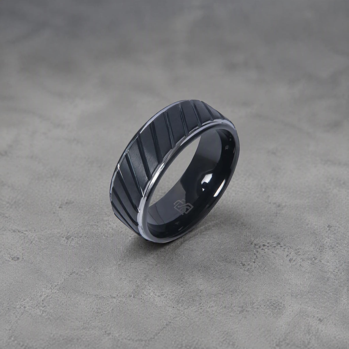 Bague en tungstène noir Ravenstone avec rainures diagonales, photographiée sur fond gris clair.