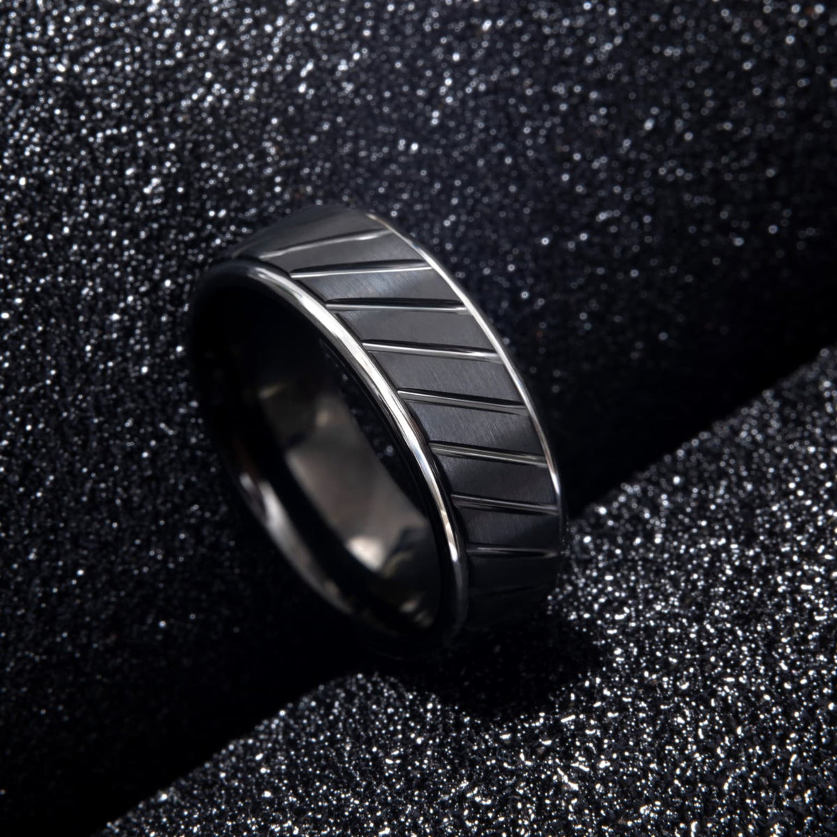 Bague en tungstène noir Ravenstone avec rainures diagonales, photographiée sur fond noir texturé.