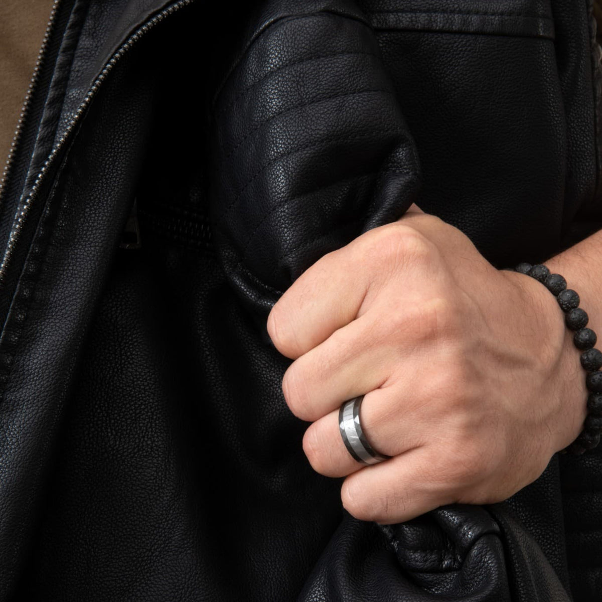 Bague Ravenstone en zirconium noir avec incrustation de météorite, portée à la main tenant une veste en cuir noir.