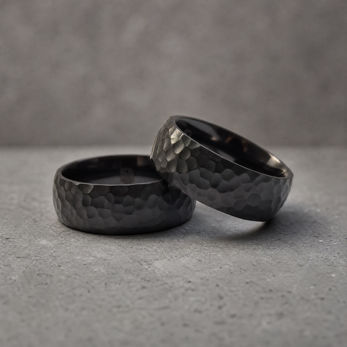 Deux bagues Ravenstone Monolith en zirconium noir martelé, posées l'une contre l'autre, illustrant l'ingénierie souveraine de la marque.