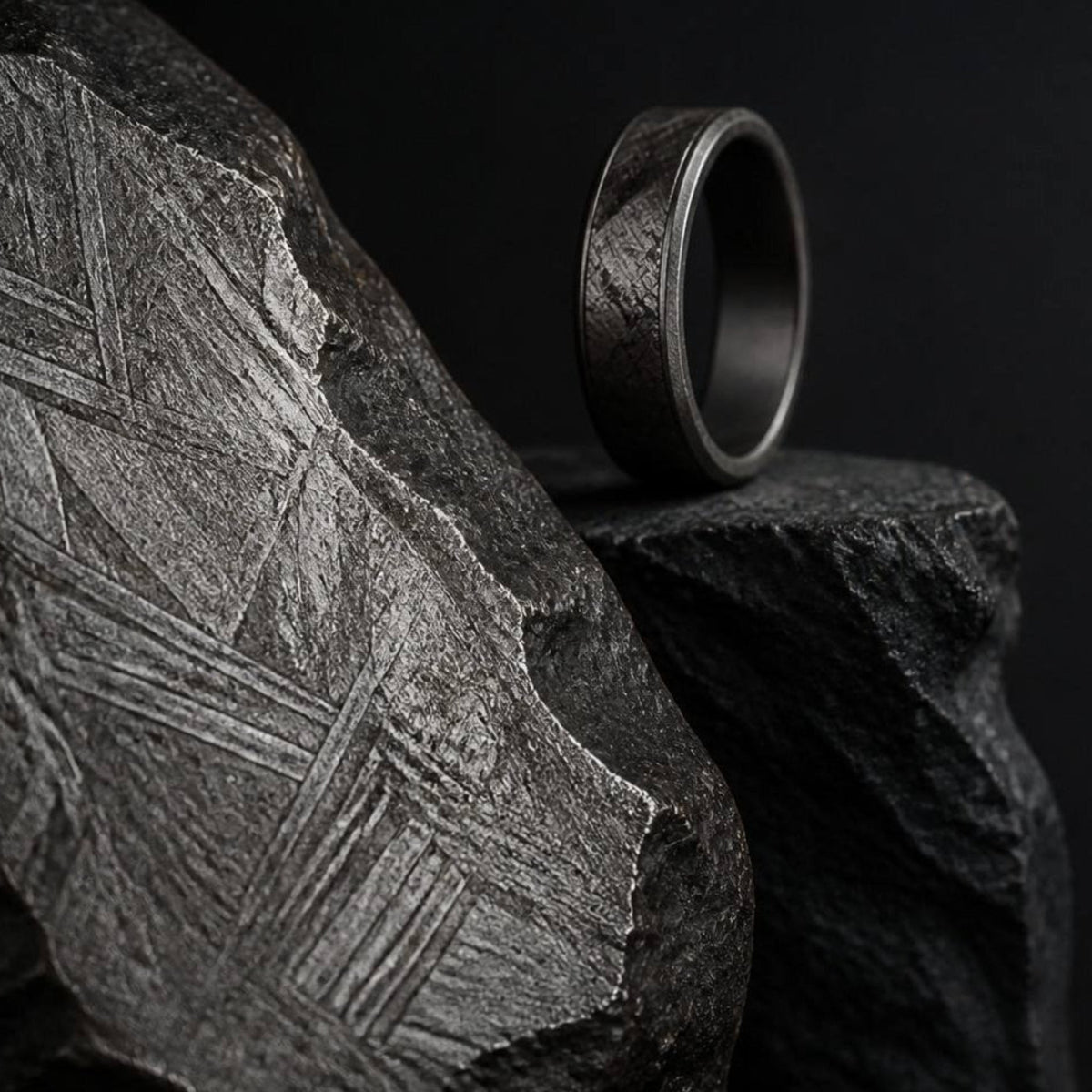 Macro d’une bague posée contre un fragment de météorite montrant des motifs Widmanstätten, révélant les textures métalliques, la structure cristalline et l’origine extraterrestre du matériau.