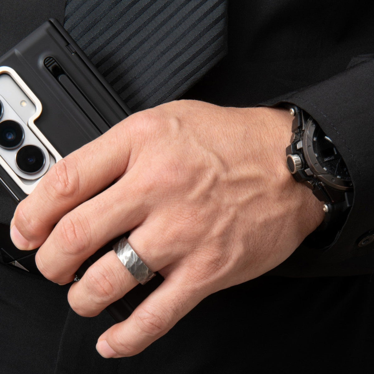Bague homme en acier damas noir à texture brossée, portée au doigt dans une mise en scène modèrne sombre.