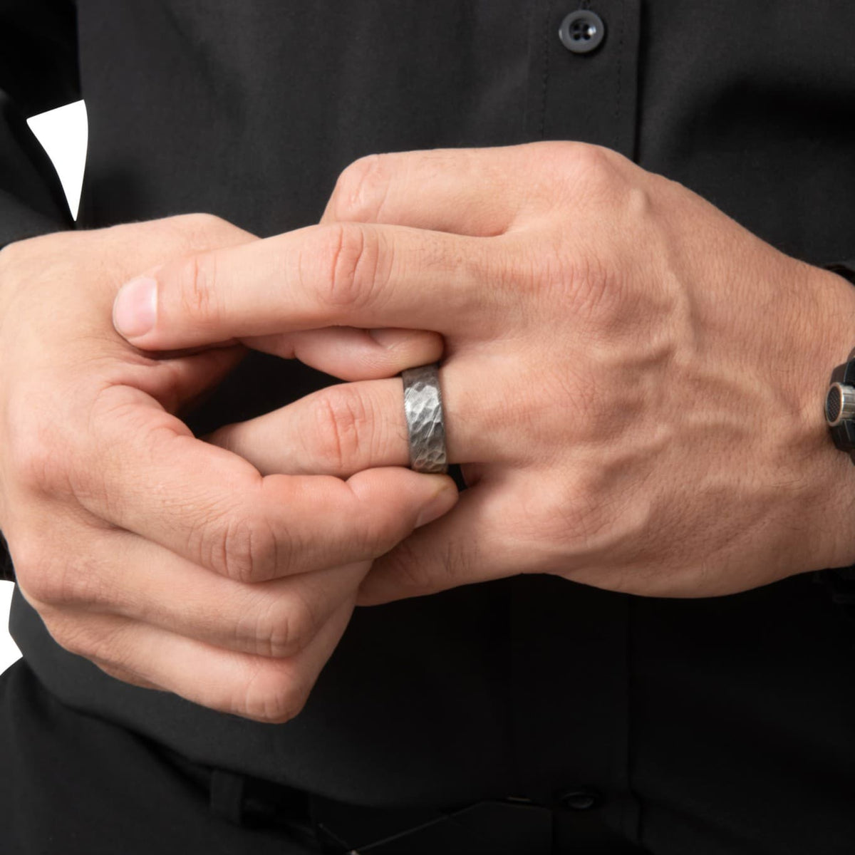 Bague Ravenstone en acier de damas martelé, portée à la main dans une scène sombre et minimaliste.
