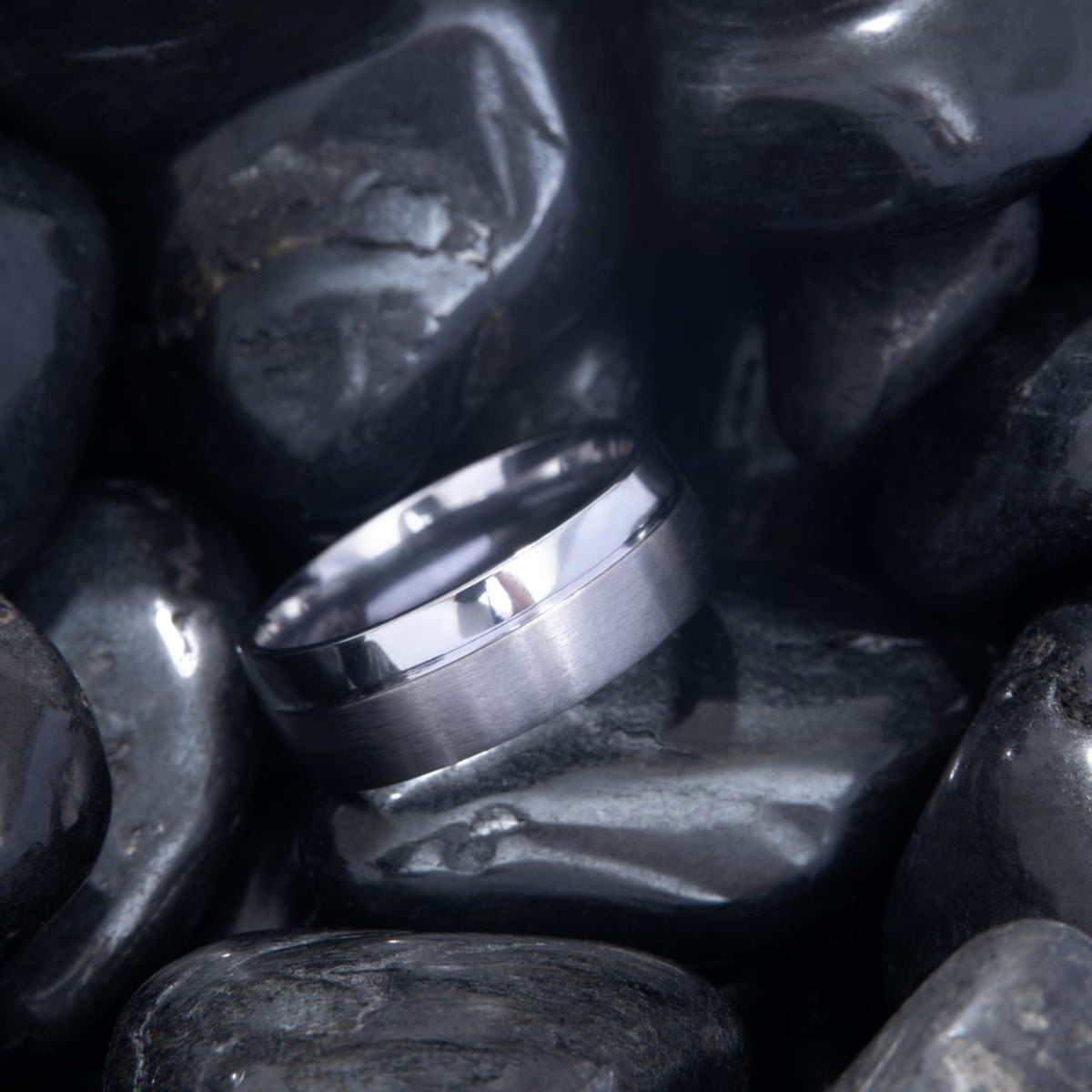 Bague Ravenstone en tantale bleu antarctique brossé avec bord lisse brillant, posée sur des pierres noires lisses.