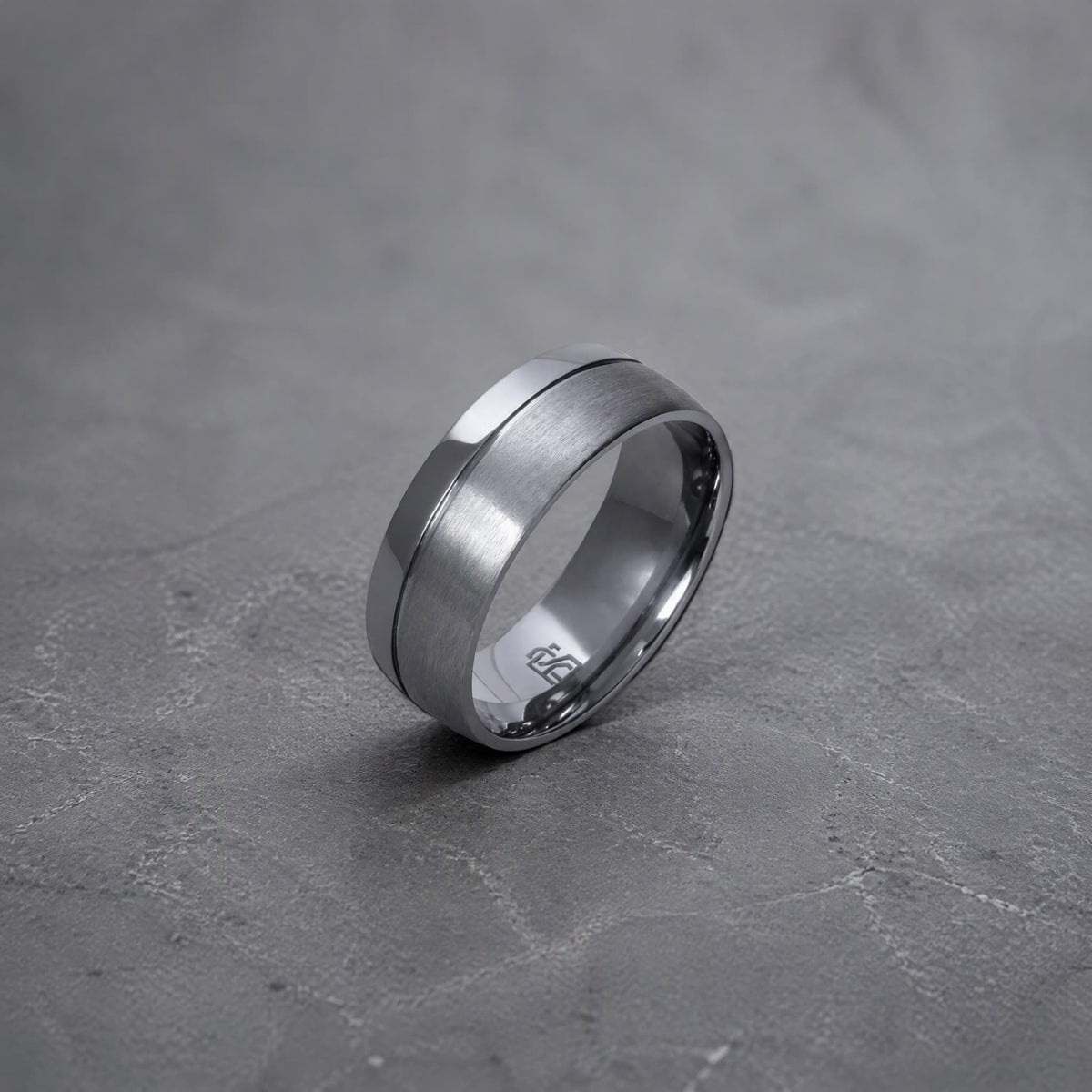 Bague Ravenstone en tantale brossé avec bord lisse brillant, posée sur un fond gris texturé.