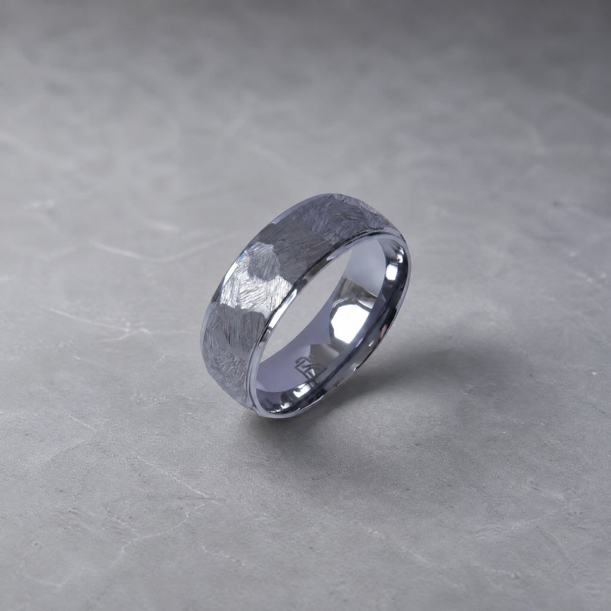 Bague Ravenstone en tantale gris martelé avec intérieur poli, posée sur un fond gris minéral.