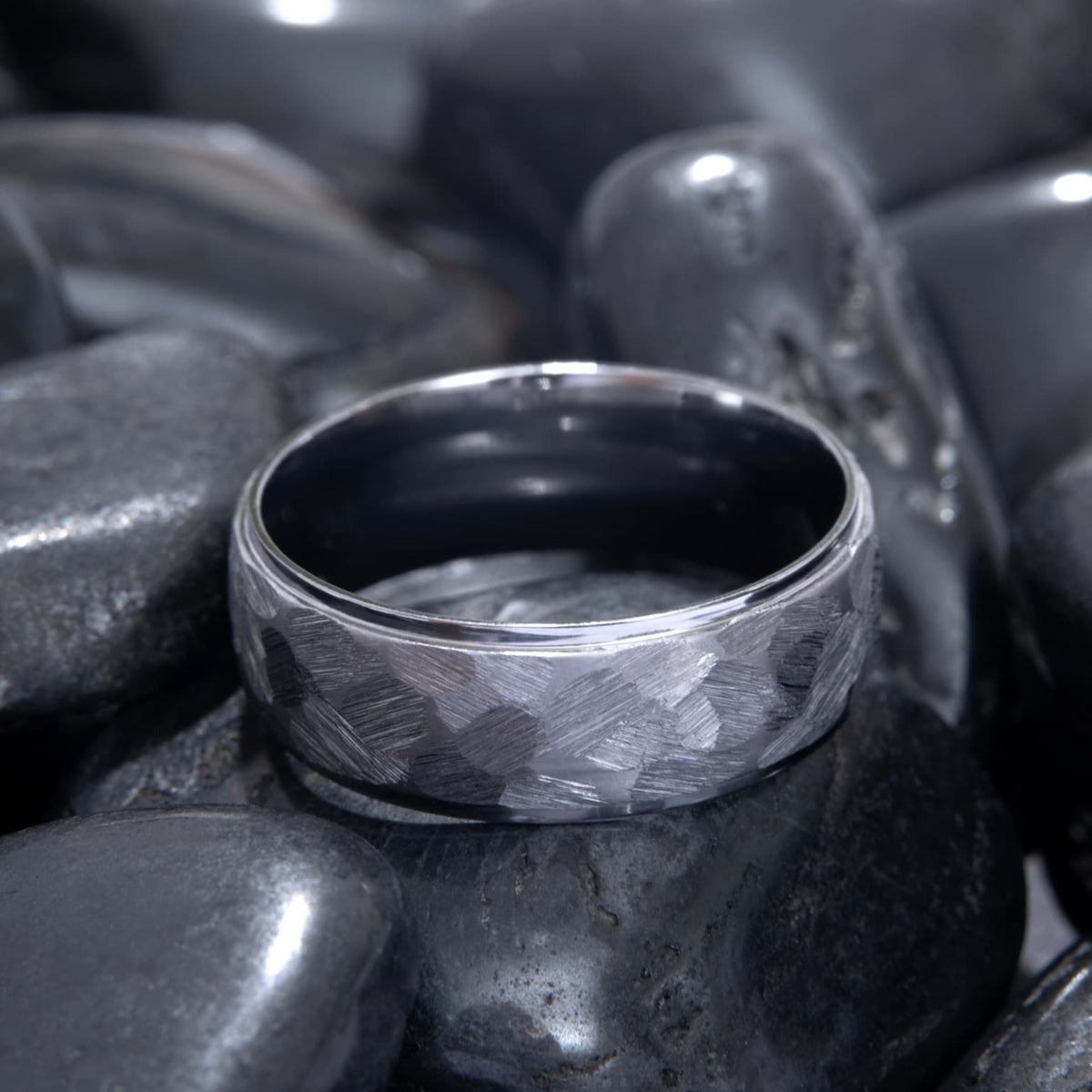 Bague Ravenstone en tantale gris martelé avec intérieur poli, posée sur des pierres noires lisses.