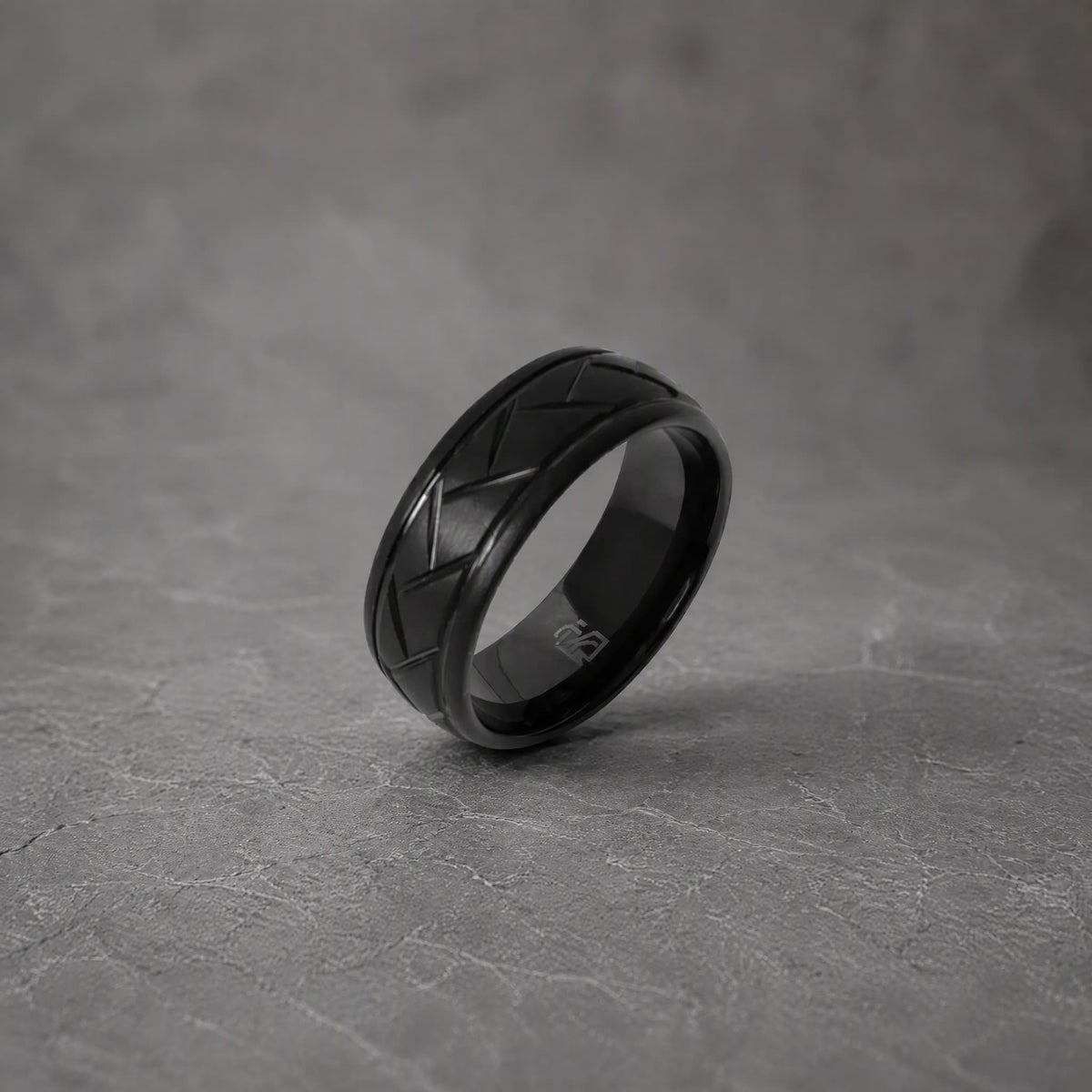 Bague en tungstène noir Ravenstone, finition mate et gravure géométrique, photographiée sur texture minérale sombre.