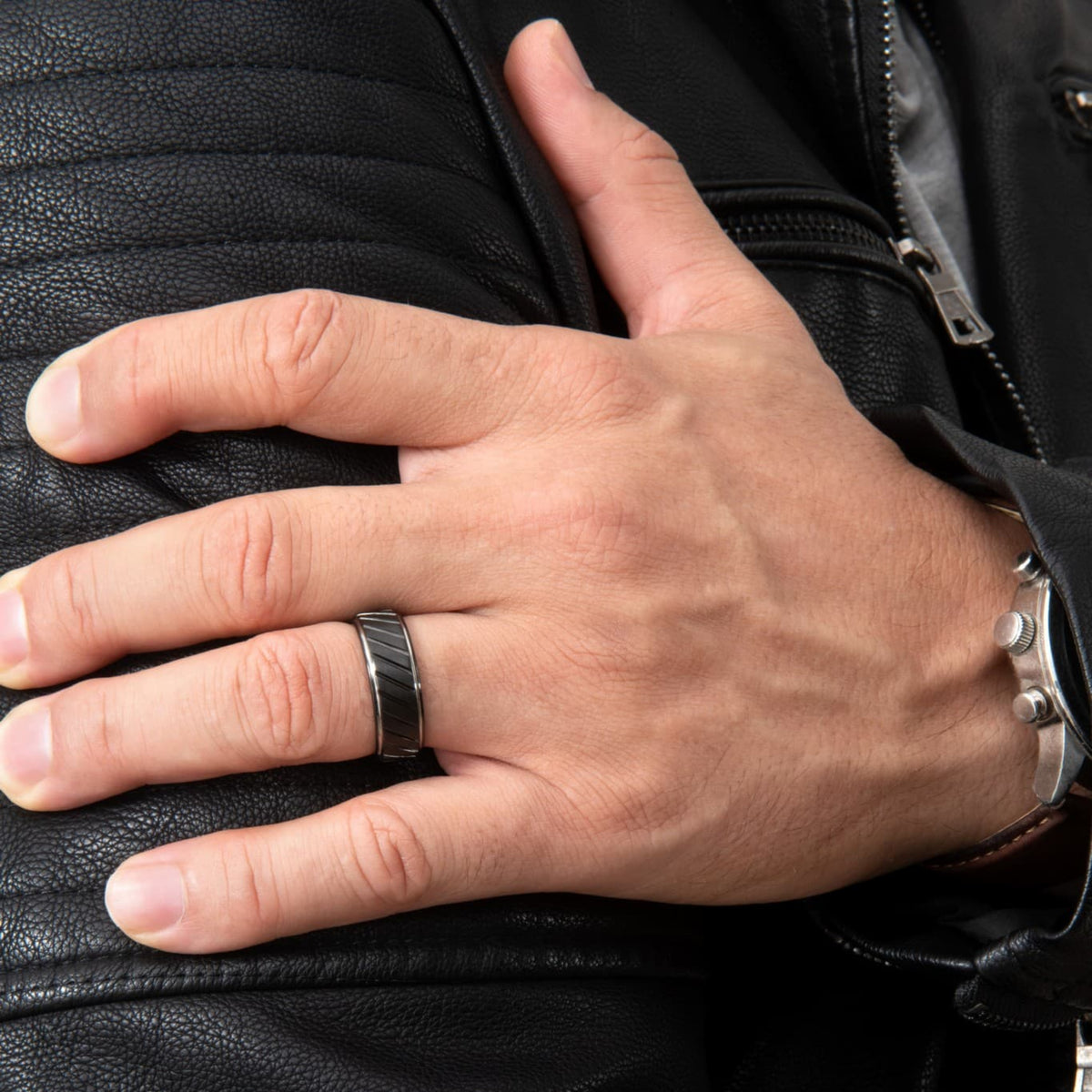 Bague en tungstène noir Ravenstone avec rainures diagonales, portée au doigt sur cuir noir.