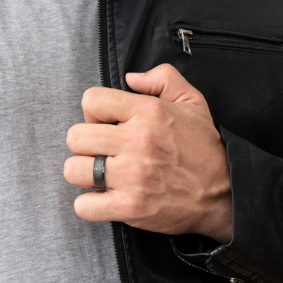 Bague Ravenstone en zirconium noir à finition brossée, portée à la main d'un homme portant une veste en cuir noir.