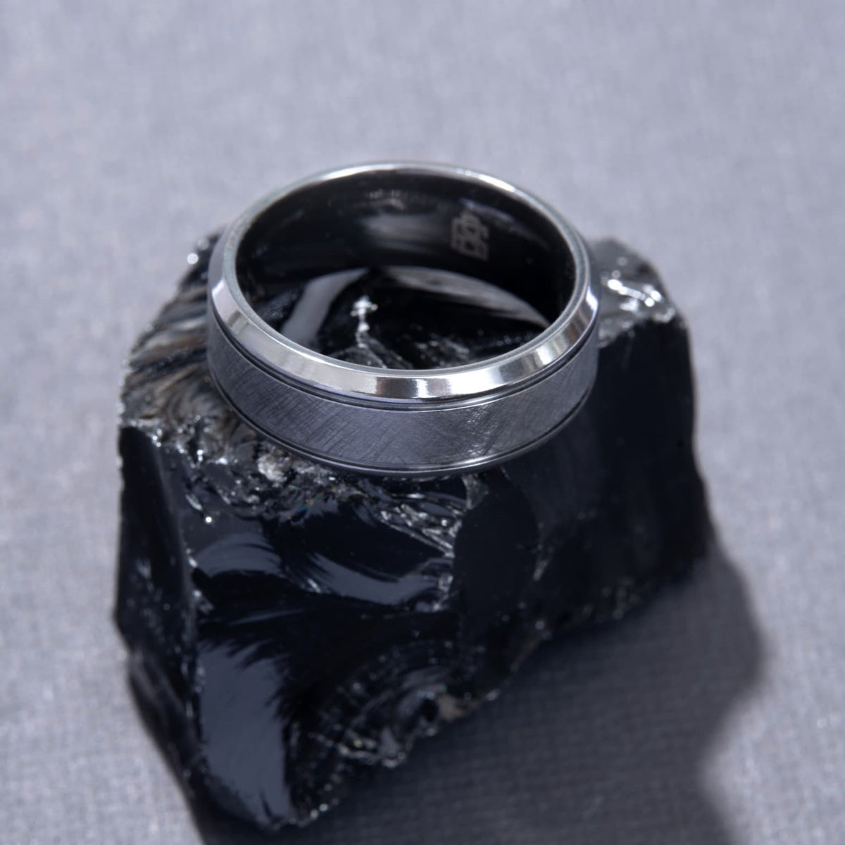 Bague Ravenstone en zirconium noir à finition brossée, posée sur une roche noire brillante.