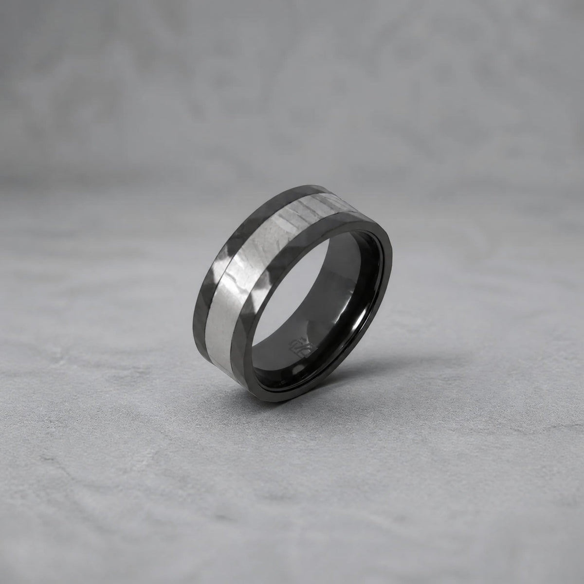Bague Ravenstone en zirconium noir avec incrustation de météorite, posée sur un fond gris texturé.