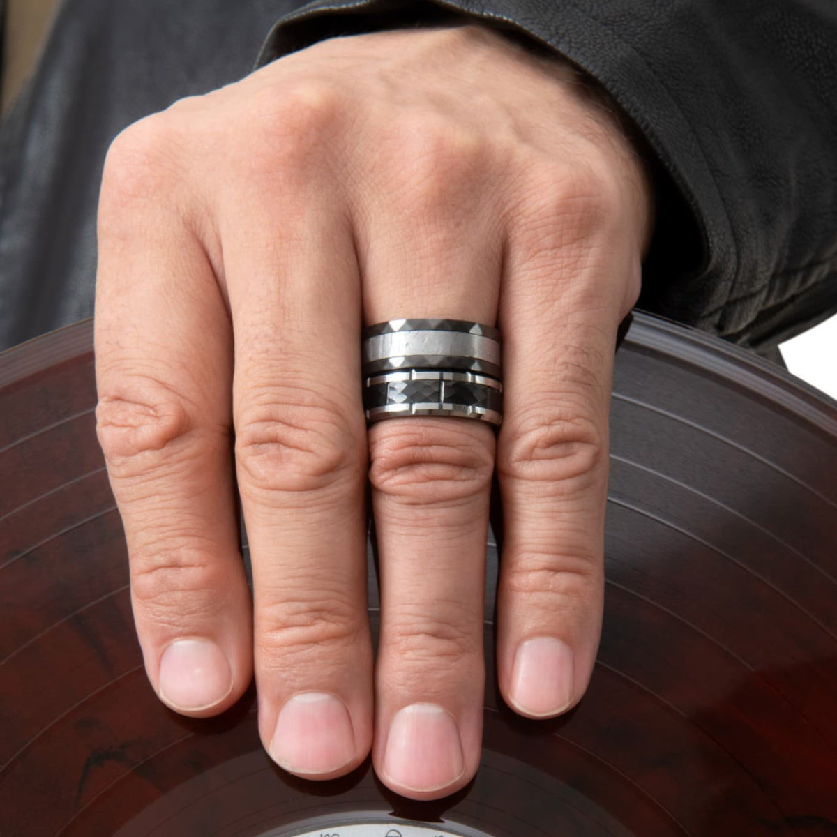Bague Ravenstone en zirconium noir avec incrustation de météorite, portée à la main posée sur un disque vinyle.