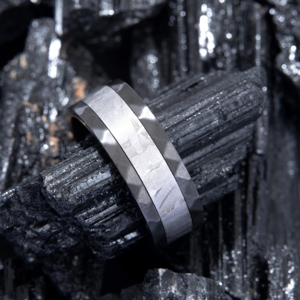 Bague Ravenstone en zirconium noir avec incrustation de météorite, posée sur des roches sombres cristallines.